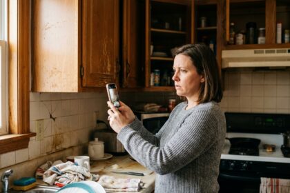 Femme utilisant son smartphone pour photographier un dégât des eaux dans sa cuisine lors d'un sinistre